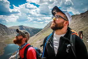 Two guys hiking on a sunny day wearing colorful, eco friendly sunscreen on their nose enjoying the adventure and looking towards the sun.